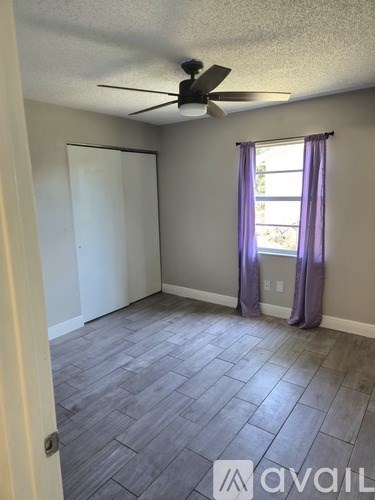 A room with a ceiling fan and a window with purple curtains.