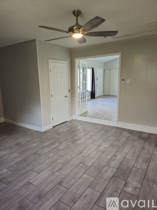 A room with a ceiling fan and light, tile flooring, and a doorway leading to another room.