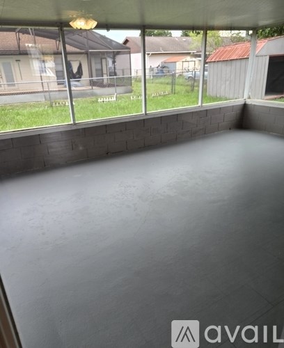 A room with a grey floor and a glass wall overlooking a backyard.