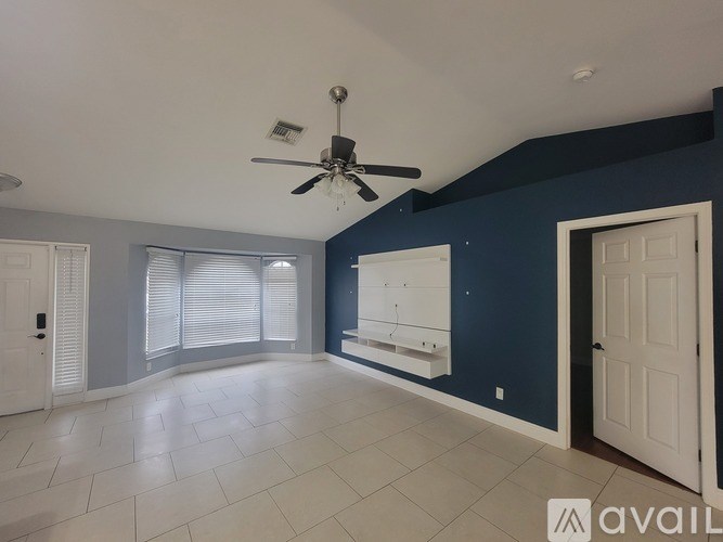 A spacious room with a ceiling fan and a large window with blinds.