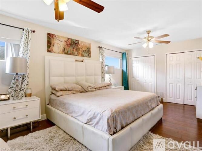 A bedroom with a large bed, a ceiling fan, and a dresser with a lamp.