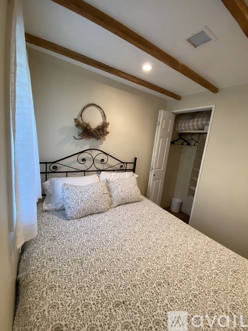 A bed with a white and beige patterned bedspread and a black metal headboard with a wreath on top.