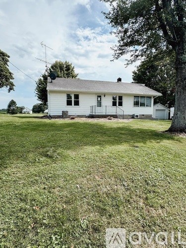 A white house with a black roof and a tree in front.