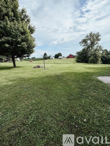 A grassy field with trees and a path leading to a red barn.