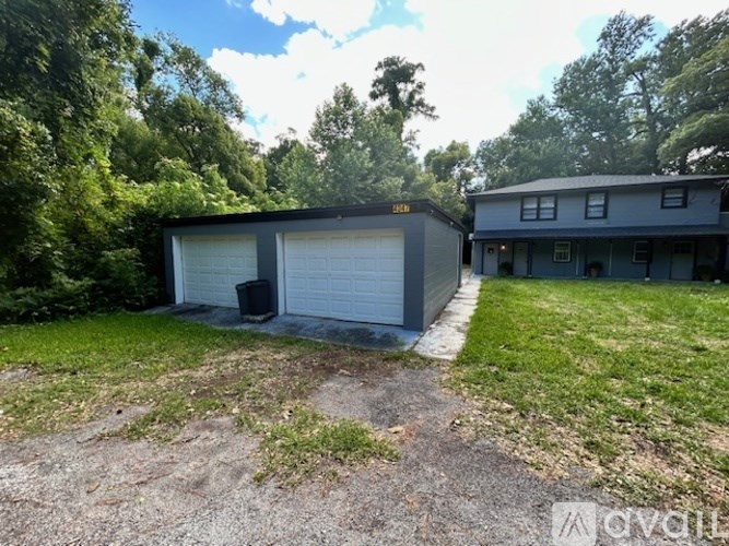 A detached garage with a white door is situated in a yard.