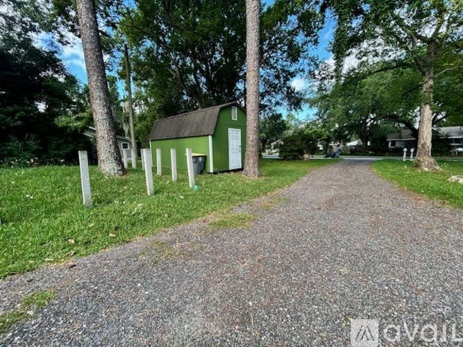 A gravel path leads to a green building with a sign in front of it.