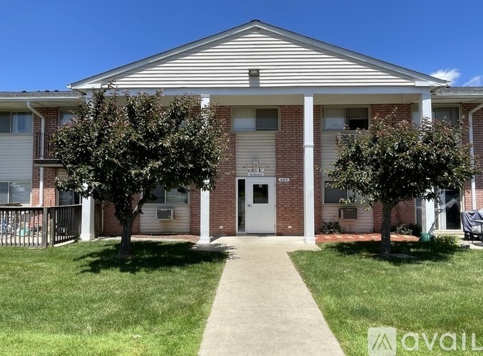 A brick building with a white door and windows, surrounded by a grassy area and trees.