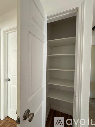 A white door with a handle and a small white cabinet with shelves is open.