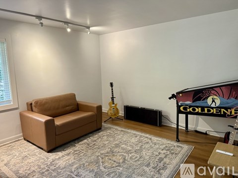 A room with a brown leather chair, a guitar, a speaker, and a poster with the word "Golden" on it.