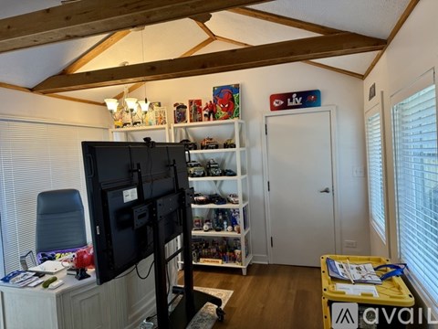 A room with a TV, a desk, and a shelf with various items.