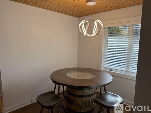 A wooden table with two chairs in front of a window with blinds.