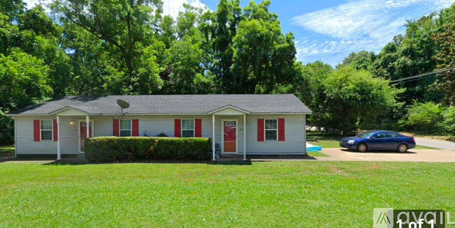 A white house with red trim and a red door is surrounded by greenery.