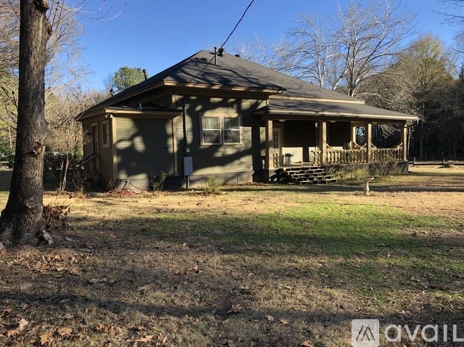 A small house with a porch is surrounded by trees and grass.