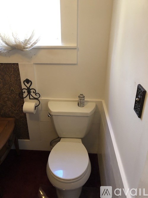 A white toilet in a small bathroom with a roll of toilet paper and a small shelf above it.