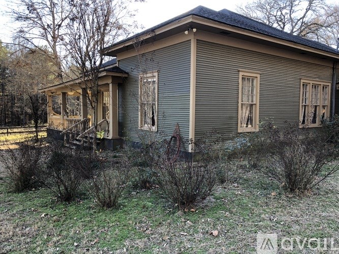 A house with a porch and a fence is surrounded by bushes.