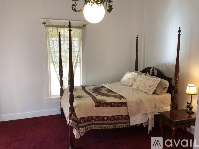 A bed with a canopy and a wooden frame is in a room with a red carpet.