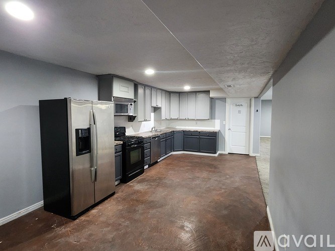 A kitchen with a black refrigerator and brown floor.