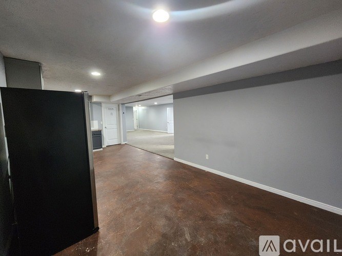 A spacious room with a black refrigerator on the left and a brown floor.