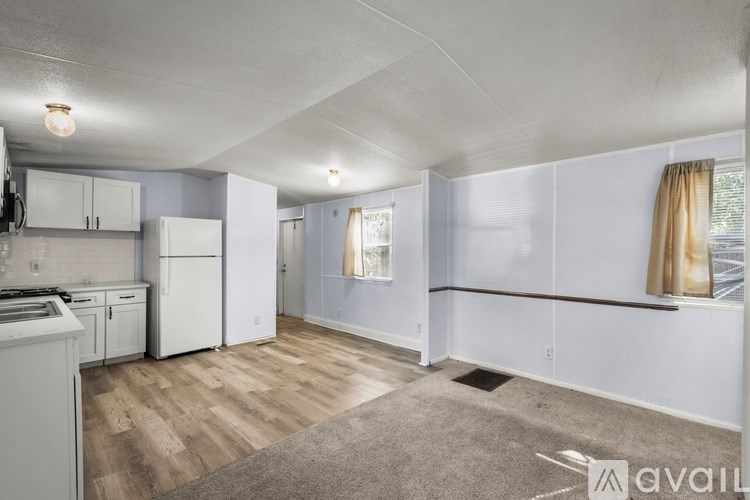 A spacious living area with a kitchen and a window with curtains.