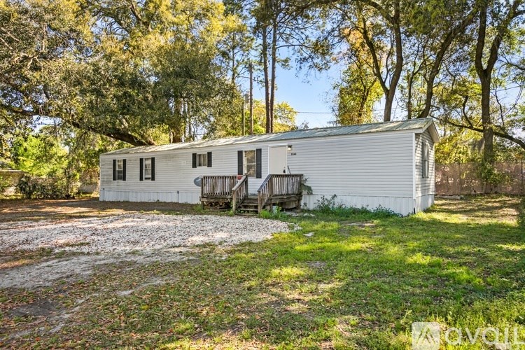 A white mobile home sits in a grassy area with trees in the background.