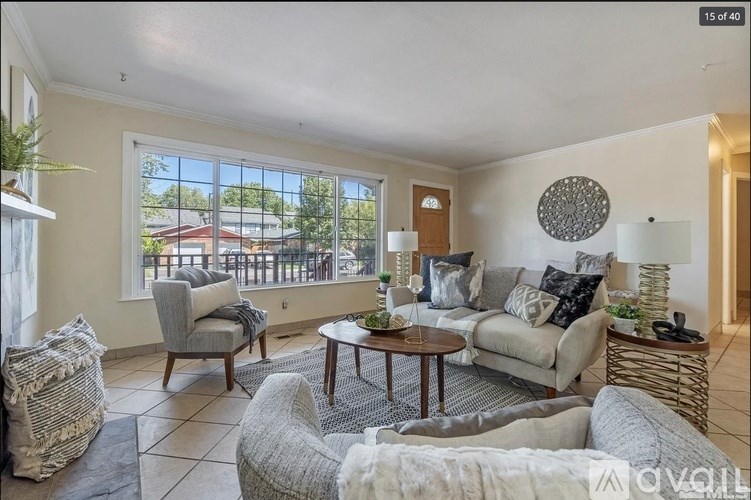 A living room with a grey sofa, a grey armchair, a wooden coffee table, and a large window with a view of a red building outside.