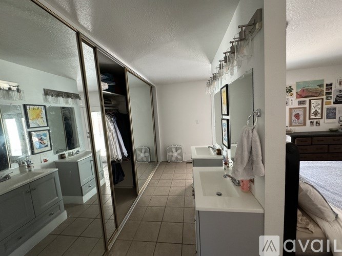 A bathroom with a sink, mirror, and a bed in the background.