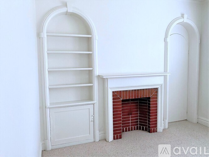 A white shelving unit sits next to a fireplace in a room with white walls.