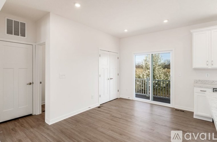 A spacious room with white walls and wooden flooring, featuring a large window with a view of the outdoors.