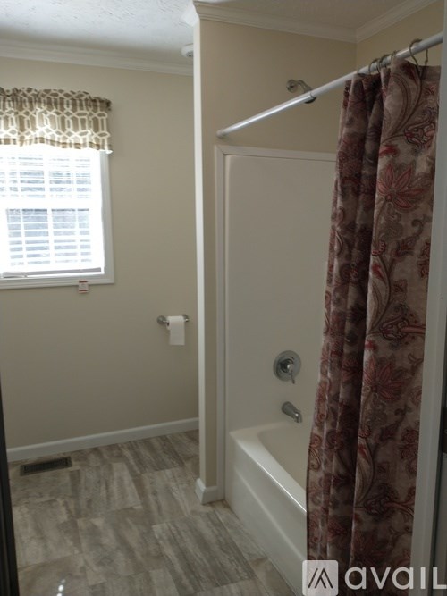 A bathroom with a tub, shower curtain, and window.