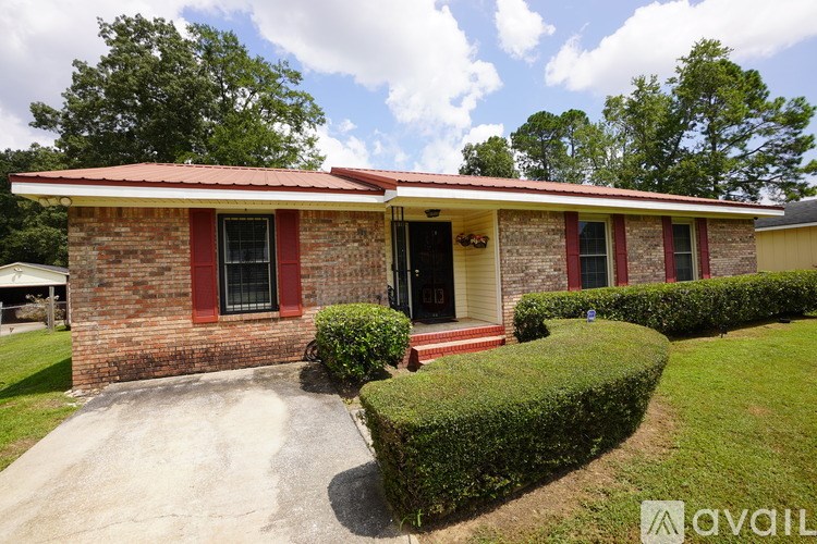 A house with a red roof and brick walls has a front yard with a hedge.