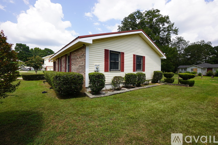 A house with a red roof and red shutters is surrounded by a green lawn and bushes.
