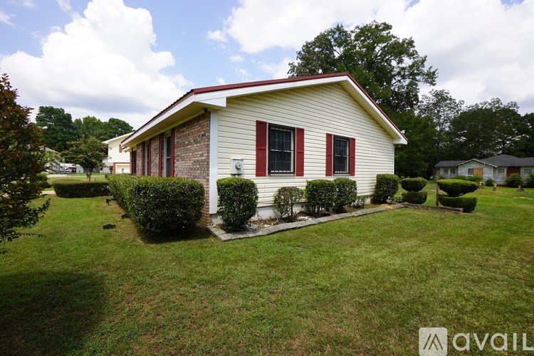A house with a red roof and red shutters is surrounded by a green lawn and bushes.