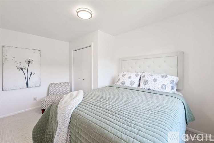 A bedroom with a bed, chair, and painting.