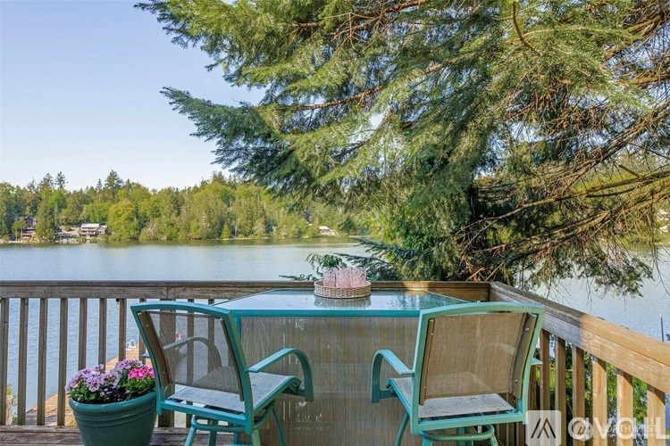 A table with chairs and flowers on a deck overlooking a lake.