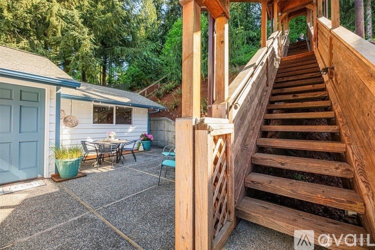 A wooden staircase leads up to a house with a blue door and a patio with a table and chairs.