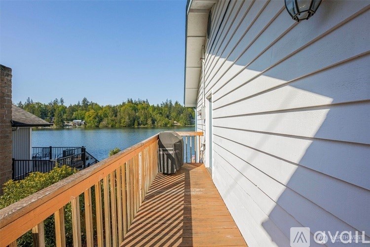 A wooden deck overlooks a body of water with a dock and trees in the distance.