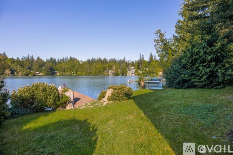 A serene lakeside scene with boats docked at a pier and lush greenery.