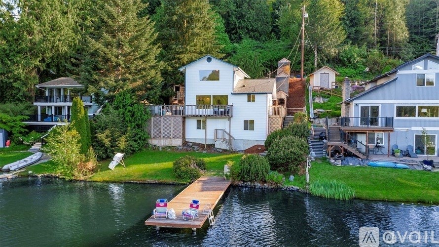 A house with a dock in front of it is surrounded by trees.