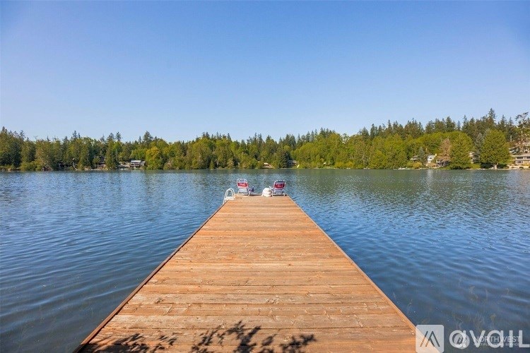A wooden dock extends into a lake with trees in the background.