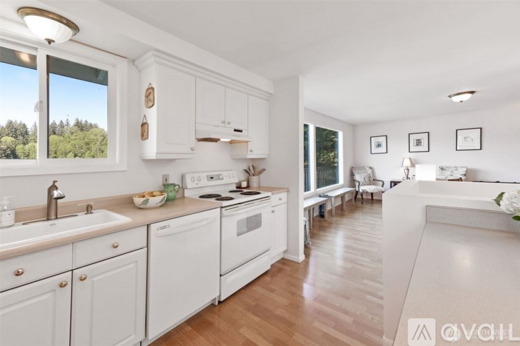 A kitchen with white cabinets and appliances, a window with a view of trees, and a dining area with a table and chairs.