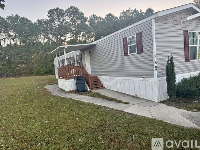 A mobile home with a porch and a small tree in front.