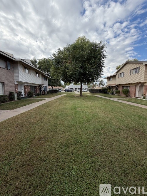 A grassy area in front of apartment buildings with a tree in the middle.