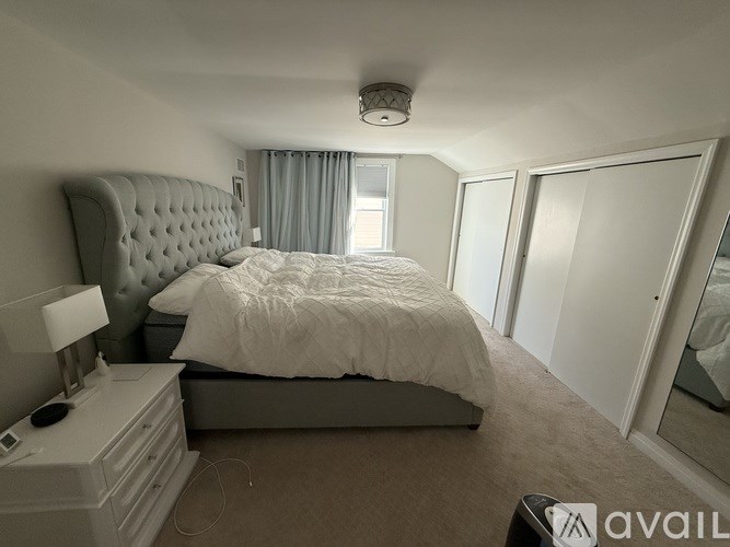 A bedroom with a large bed, a nightstand with a lamp, and a window with curtains.