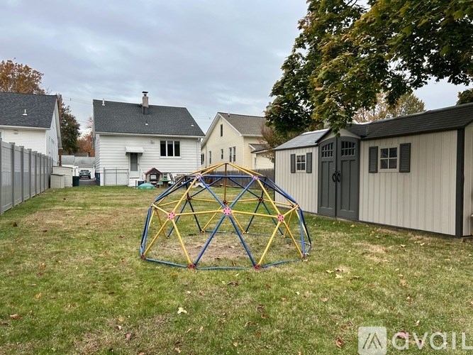 A play structure sits in a yard in front of a white house.