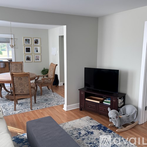 A living room with a grey sofa, a wooden rocking horse, a wooden chair and a television.