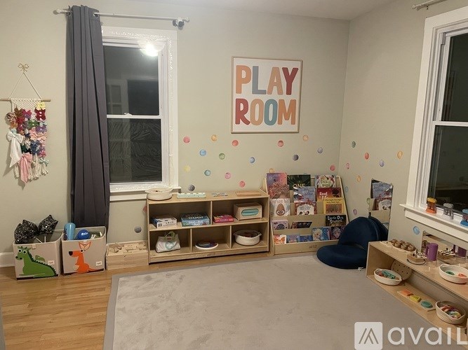 A play room with a grey carpet and a wooden shelf with toys.