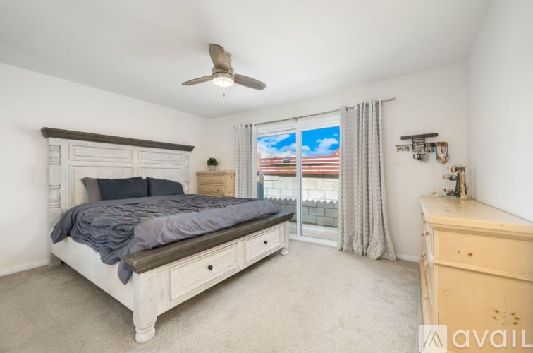 A bedroom with a large bed, a ceiling fan, and a window with a view of the city.