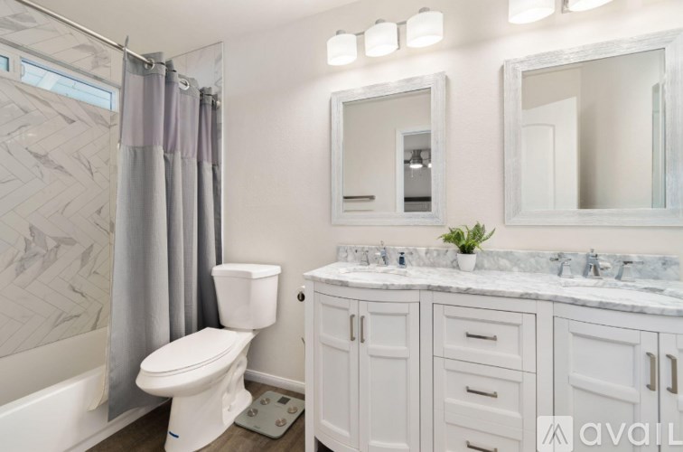 A bathroom with a white toilet, a white sink, and a white bathtub with grey curtains.