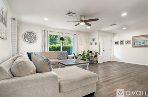 A living room with a beige couch and a ceiling fan.