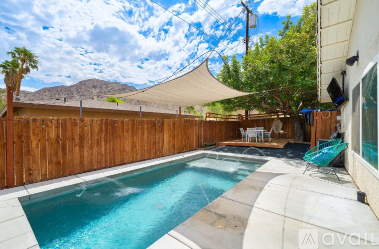 A pool with a wooden fence and a patio with chairs.